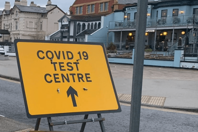 A picture of a yellow sign reading 'covid 19 test centre' on a New Brighton background