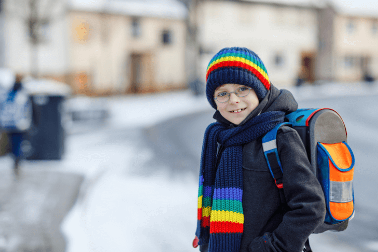 Young boy wearing colourful scarf and hat as well as reflective patches on his backpack so that they can be more visible in darker or foggier weather