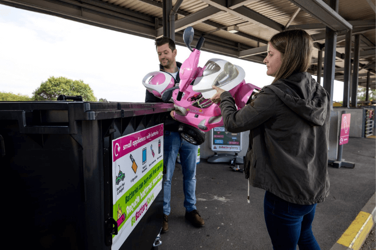 Two people placing a child's large toy into a recycling point at the tip
