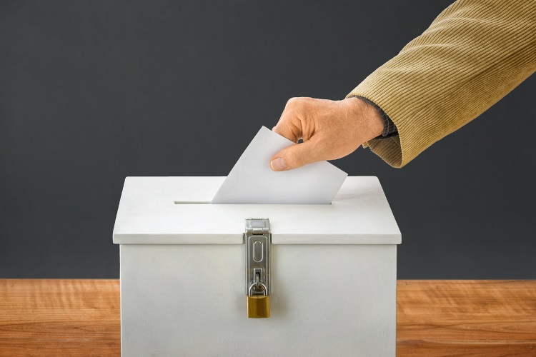 Stock image of a person's hand casting a vote into a ballot box