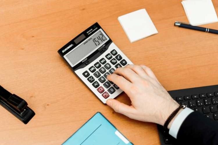 photo shows a hand using a calculator on a desk