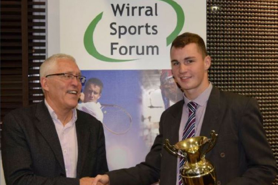 A winner of the Wirral Sports Awards shaking hands with somebody in front of a Wirral Sports Forum banner