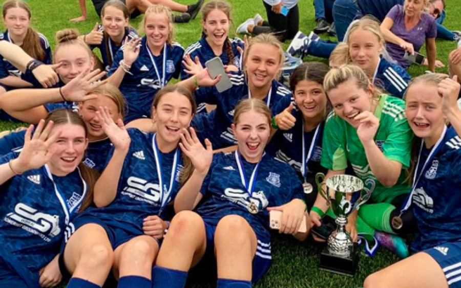 Glanavon Belles - the winners of the Under 15/16s Group. Group of young women wearing blue football kit laying down celebrating with silver cup in Leasowe Wirral