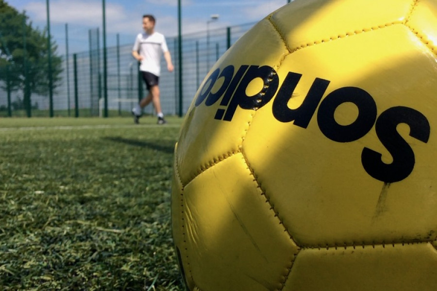 Close-up of a yellow football in the foreground, with a player shown out of focus in the background