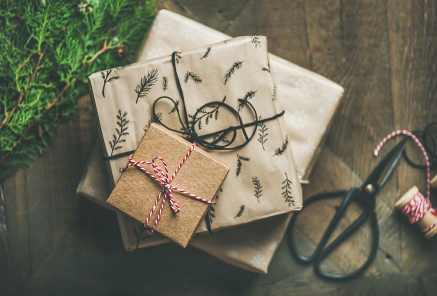 A small stack of presents from above and the presents are wrapped in brown paper with a pine leaf design on one and a string ribbon