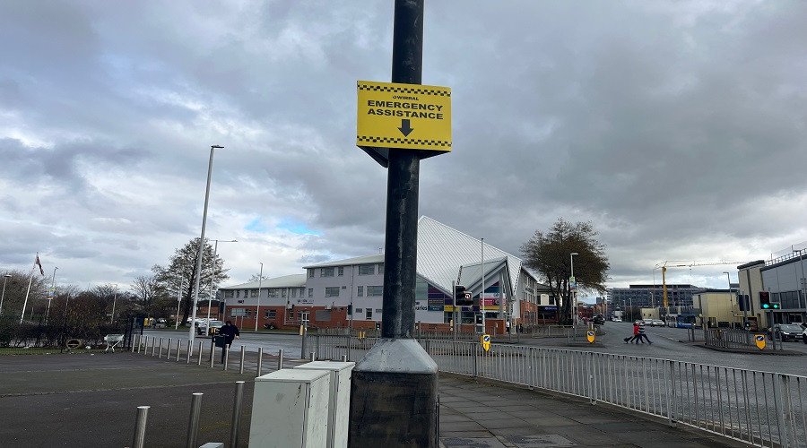 yellow help point sign attached to black cctv column next to a busy junction