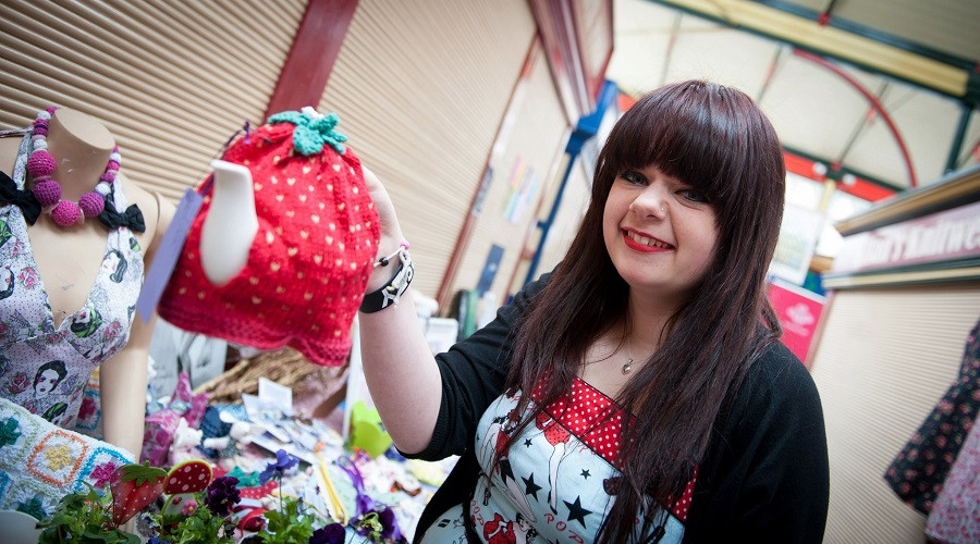 a young trader holding up a hand-knitted tea cosy in the design of a strawberry