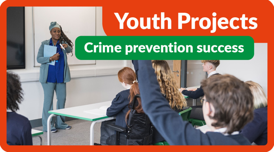 Classroom with black woman talking at the front of the class and a group of youths listening and one boy raising his hand - text on graphic says Youth Projects - Crime prevention success