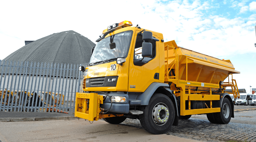 A yellow gritting truck pulled up in front of a salt dome