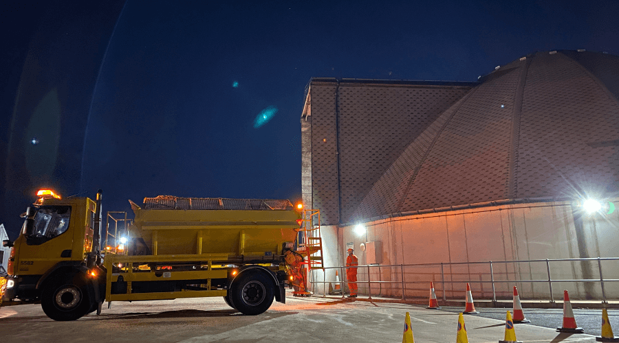 A yellow gritting vehicle parked alongside the salt dome ready to be loaded with salt.