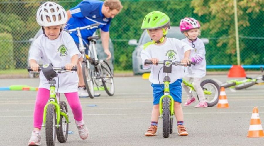 Three young children riding balance bikes around mini traffic cones.