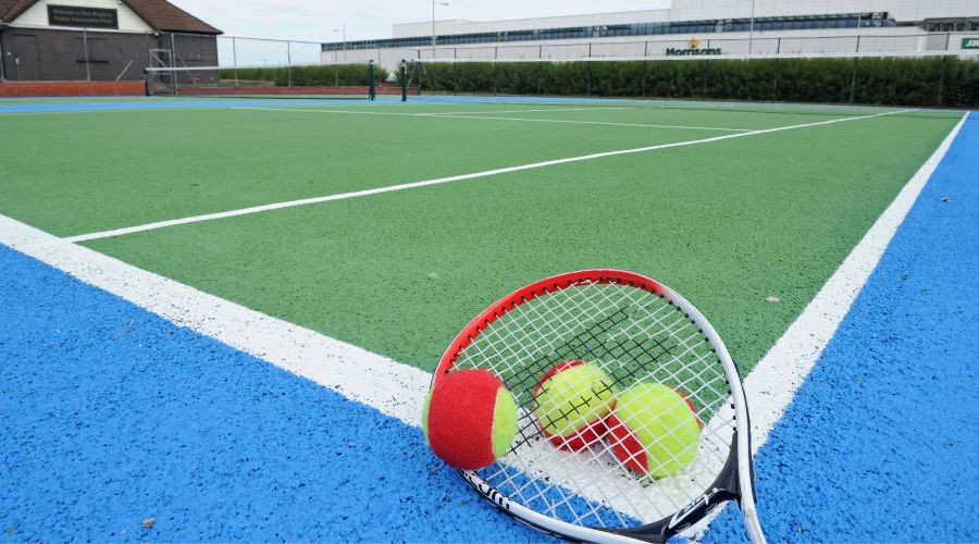 A tennis racket and balls on the ground of a newly re-painted tennis court.