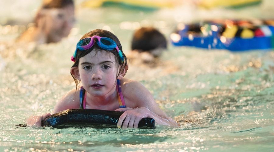 Girl wearing googles leaning on a float in a busy swimming pool