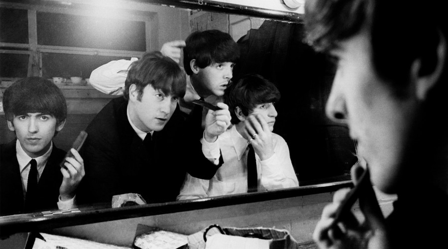 Four members of The Beatles look at their own reflection in a mirror