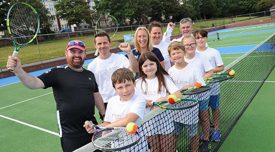 A group of young people wearing Active Wirral t-shirts holding tennis rackets on a revamped court