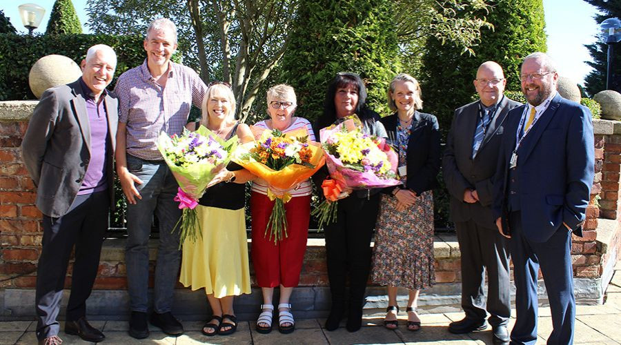 A group photo of foster carers and others holding flowers at an appreciation event.