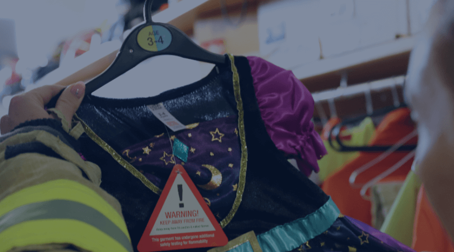 A halloween costume being held up and looked at by a member of the fire service and that has a tag on it that says 'flammable'