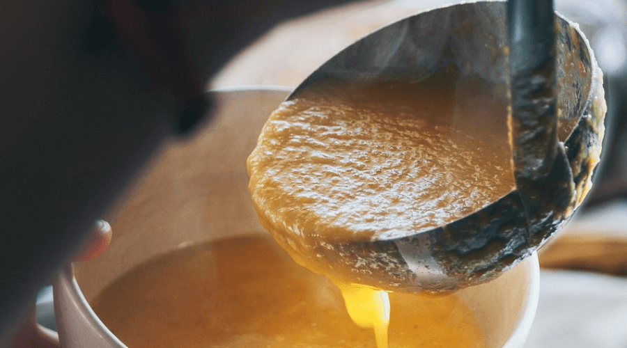 Close up of a ladle scooping soup into a bowl