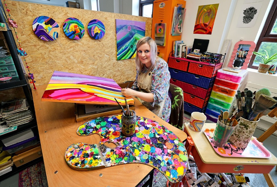 Gweni-Louu, a visual artist sits in her studio painting in bright colours