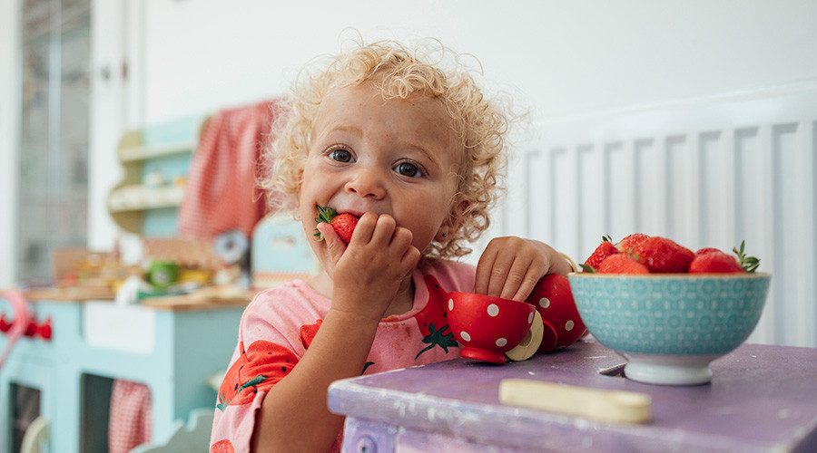 Toddler with curly blonde haie eating strawberries from a bowl