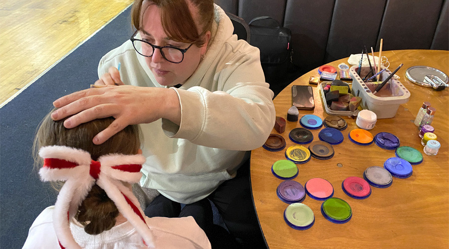 A woman painting a child's face, the child's face is obscured