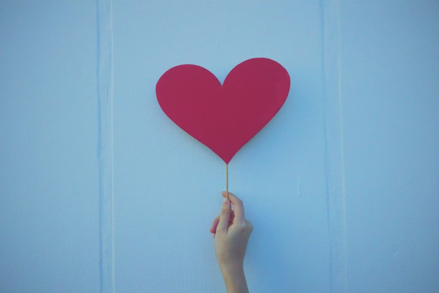 A hand holding up a red paper heart on a stick in front of a red background