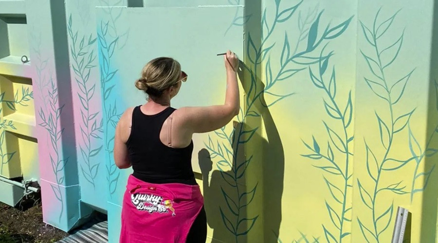 woman artist painting a mural on a blue wall