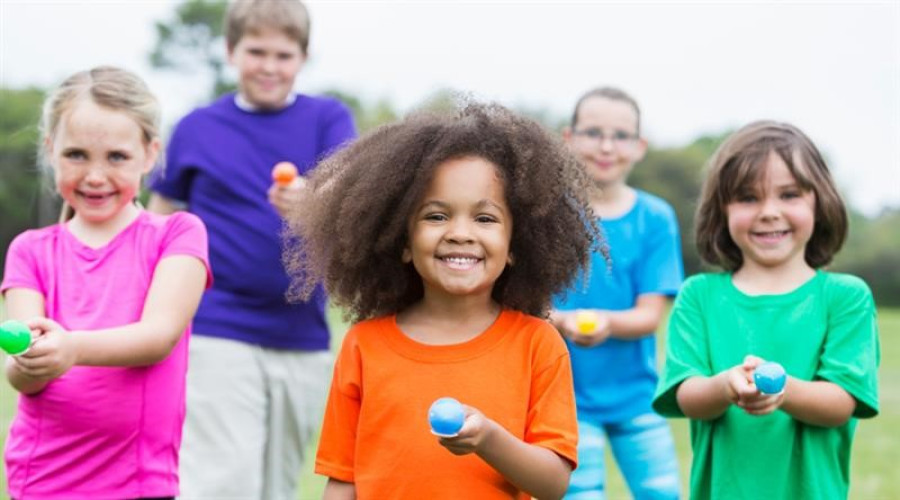 pic of 5 children smiling to camera in colourful tops holding eggs on spoons