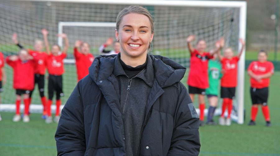 Niamh Charles close up in front of goal with girls football team lined up