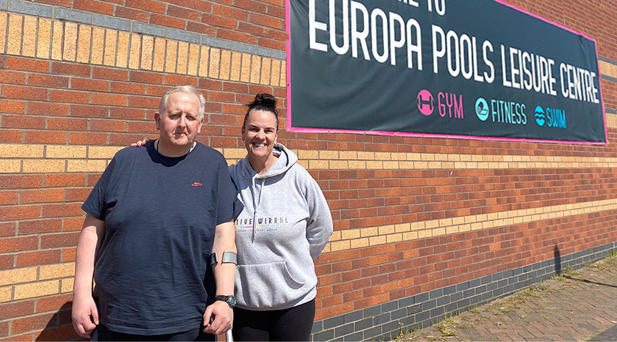 Barry and Sonia from Active Wirral team standing outside under a Europa Pools Leisure Centre banner
