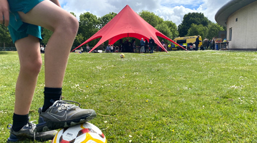 Close up of youth foot balancing on football with the Fostering big red tent in distance 