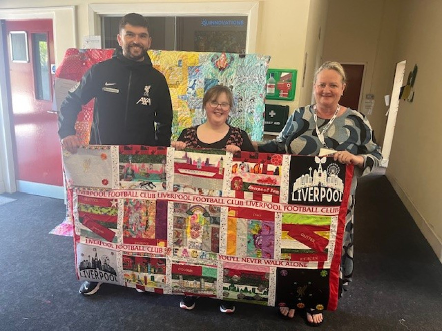 Three people holding up a handmade quilt. They are all smiling.