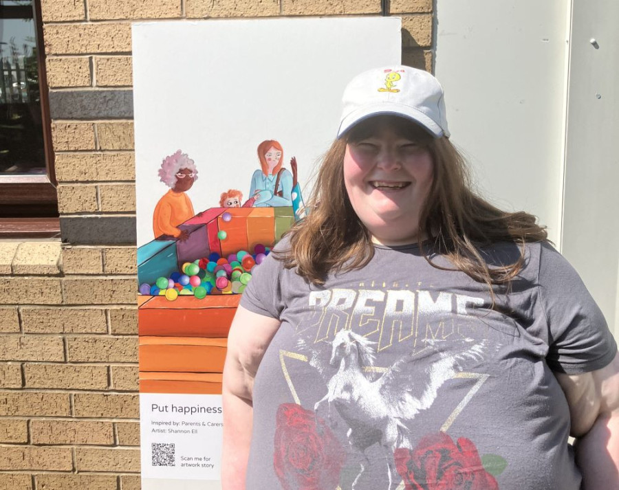 A young lady in a grey t shirt and white cap standing next to an art board. She is smiling.