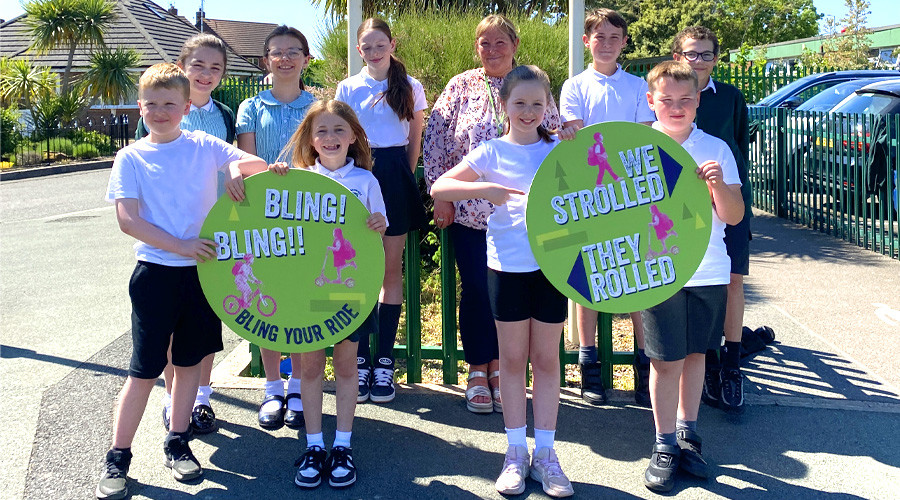 Children and adults from Greenleas school holding green signs promoting walking, cycling, and scooting to school, outside a residential area
