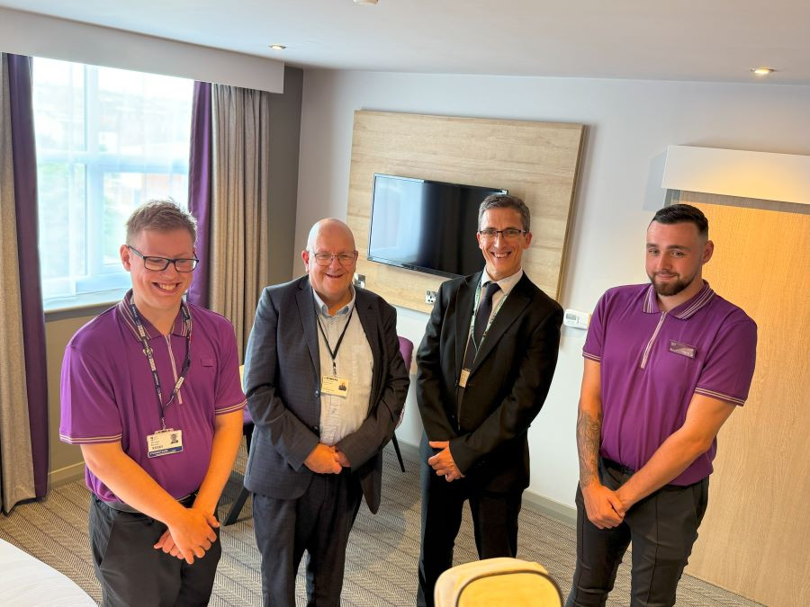 Two men in grey suits standing in between two students in Premier Inn uniforms.