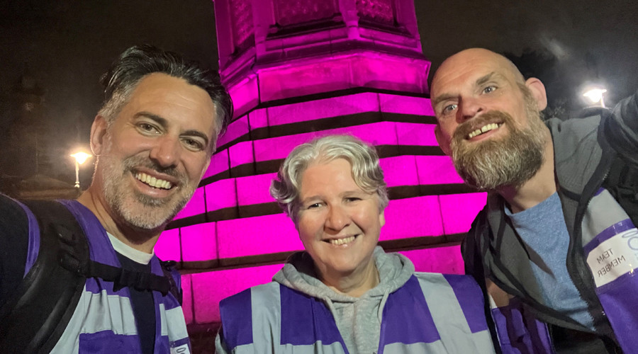 picture of three smiling volunteers wearing purple bibs at night