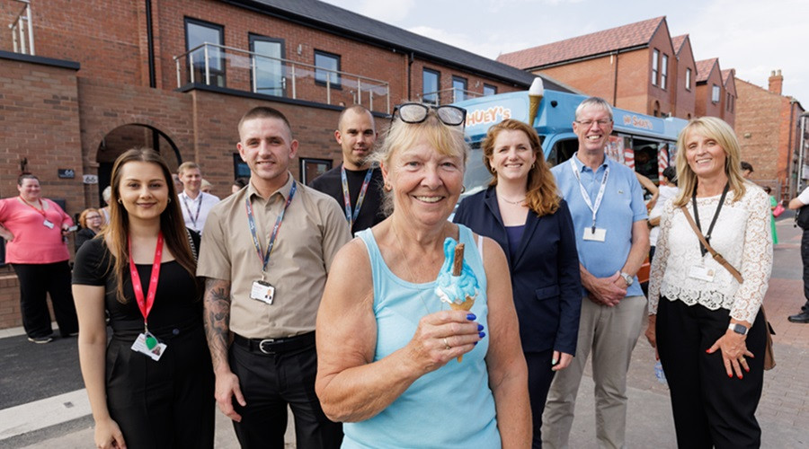 Group of people outside new apartments in New Ferry. A woman in front holding an ice cream cone.