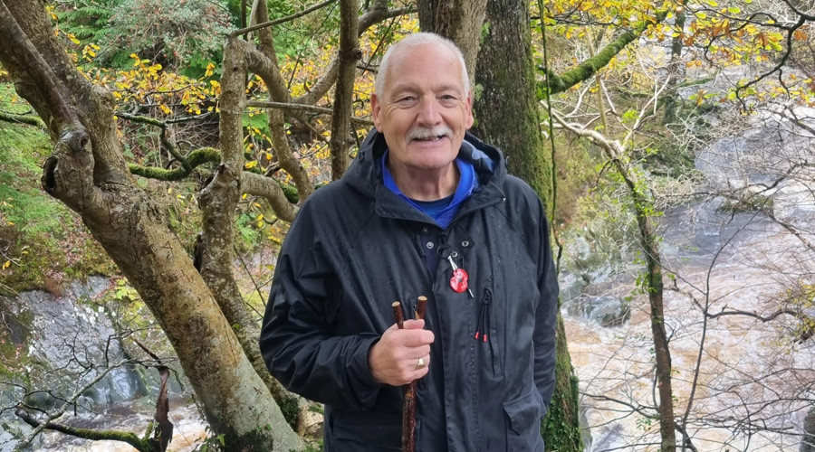 Senior man with holding walking stick, smiling at camera, next to the river on sunny autumn day