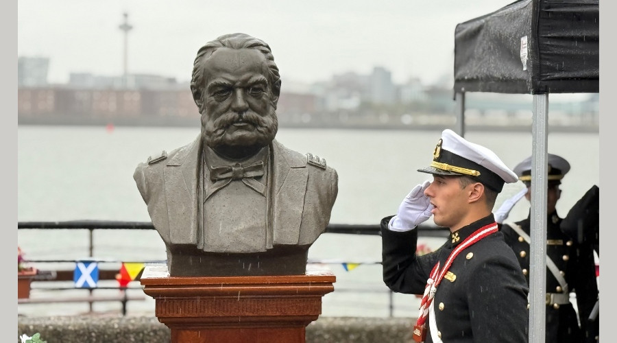 Photo of a member of the crew of BAP Union saluting next to a bust of Grand Admiral Miguel Grau