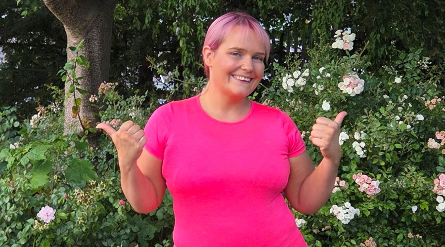 Young women with pink hear wearing bright pink top - jestering thumbs up