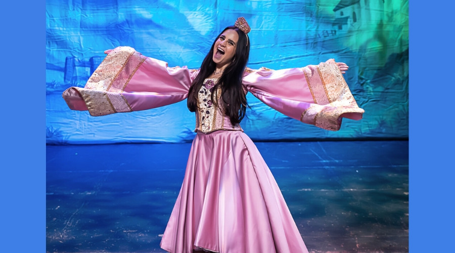 Photo of Cleo Demetriou with her arms stretched out on stage in the costume of Princess Rose
