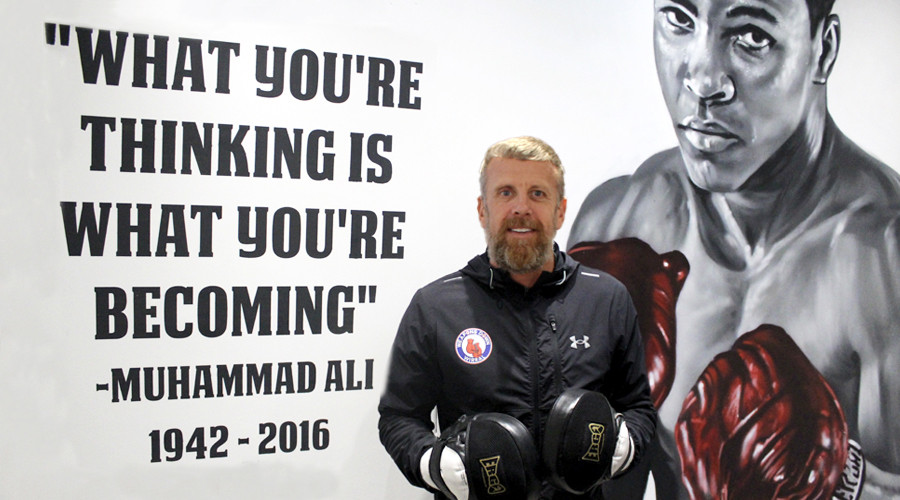 Andy from Argyle Community Fitness standing in front of mural of Muhammad Ali with quote "What you're thinking is what you're becoming""