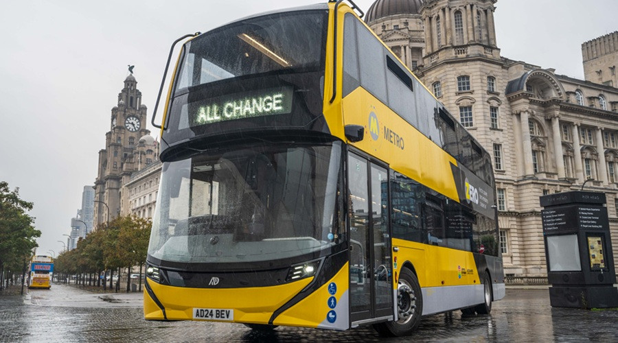 a new metro bus pictured in front of Liverpool's 3 graces, in bright yellow with "all change" where the number usually is