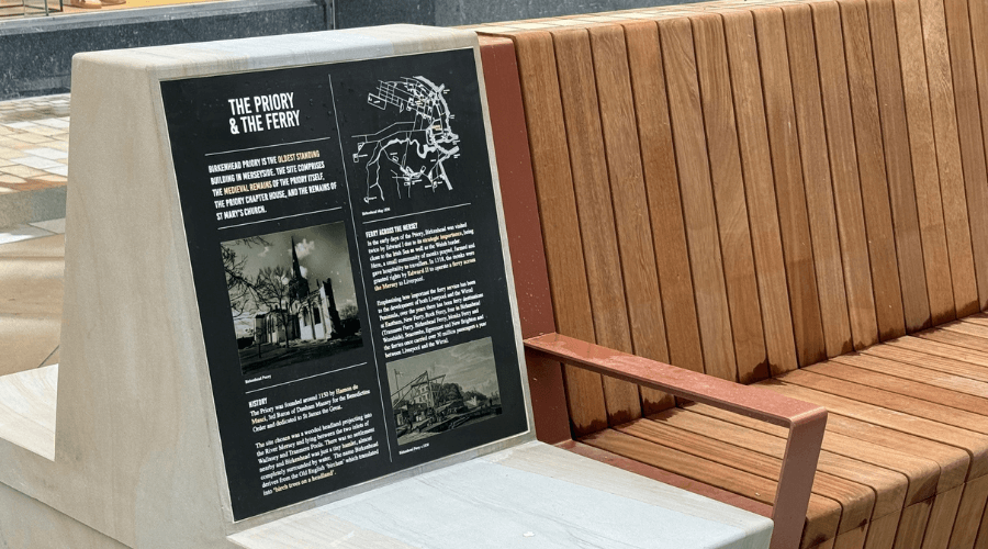 Close up of one of the stone and timber benches where you can see a plaque with information on about the priory and the ferry in Birkenhead