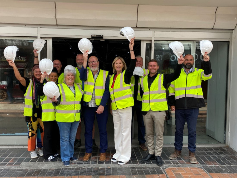 Councillors, traders and construction workers stand outside the former TJ Hughes unit wearing high vis jackets and holding their hard hats in the air