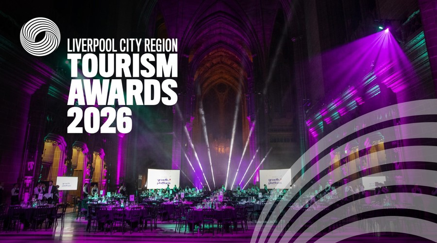 Liverpool City Region Tourism Awards 2026 event inside a large cathedral-like venue, illuminated with purple and teal stage lighting. Banquet tables fill the hall beneath dramatic spotlights, with the Tourism Awards 2026 branding displayed prominently on the left and a graphic motif in the lower right corner.
