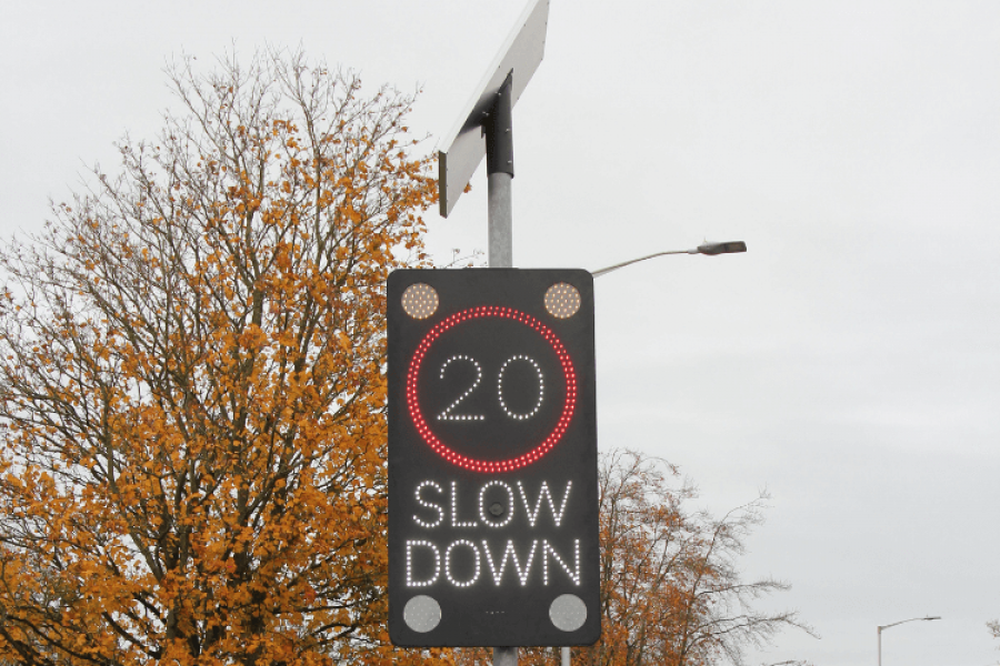 Close up of one of the traffic signs installed - it is a black sign with LED lights that will shine if cars are going too quickly to illuminate the 20mph speed limit and the words 'slow down' and a solar panel at the top which powers the sign