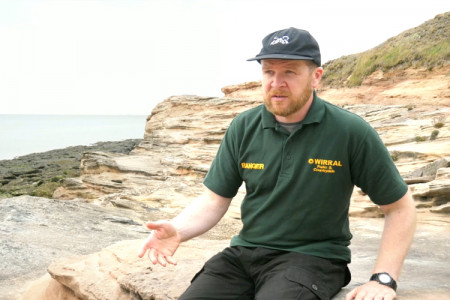 Wirral Country Park Ranger Matt sat on rocks next to the coast
