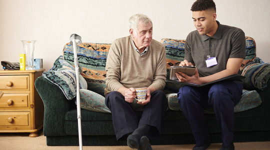 Young man and older man sitting on sofa looking at looking at ipad discussing services available in Wirral's social care