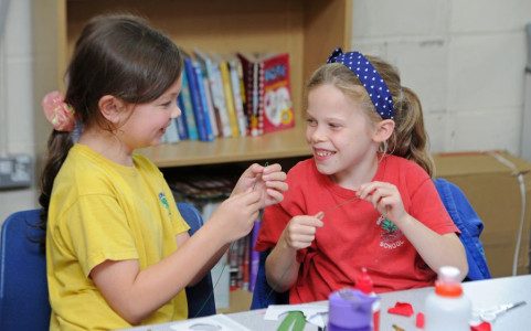 Two children taking part in the workshop smiling at each other as they create the wildflowers